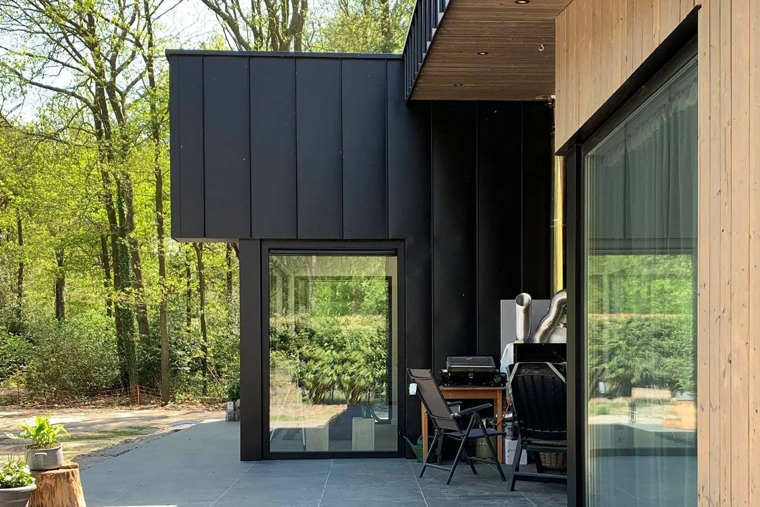 Glazed building facade and sheltered terrace beside trees.