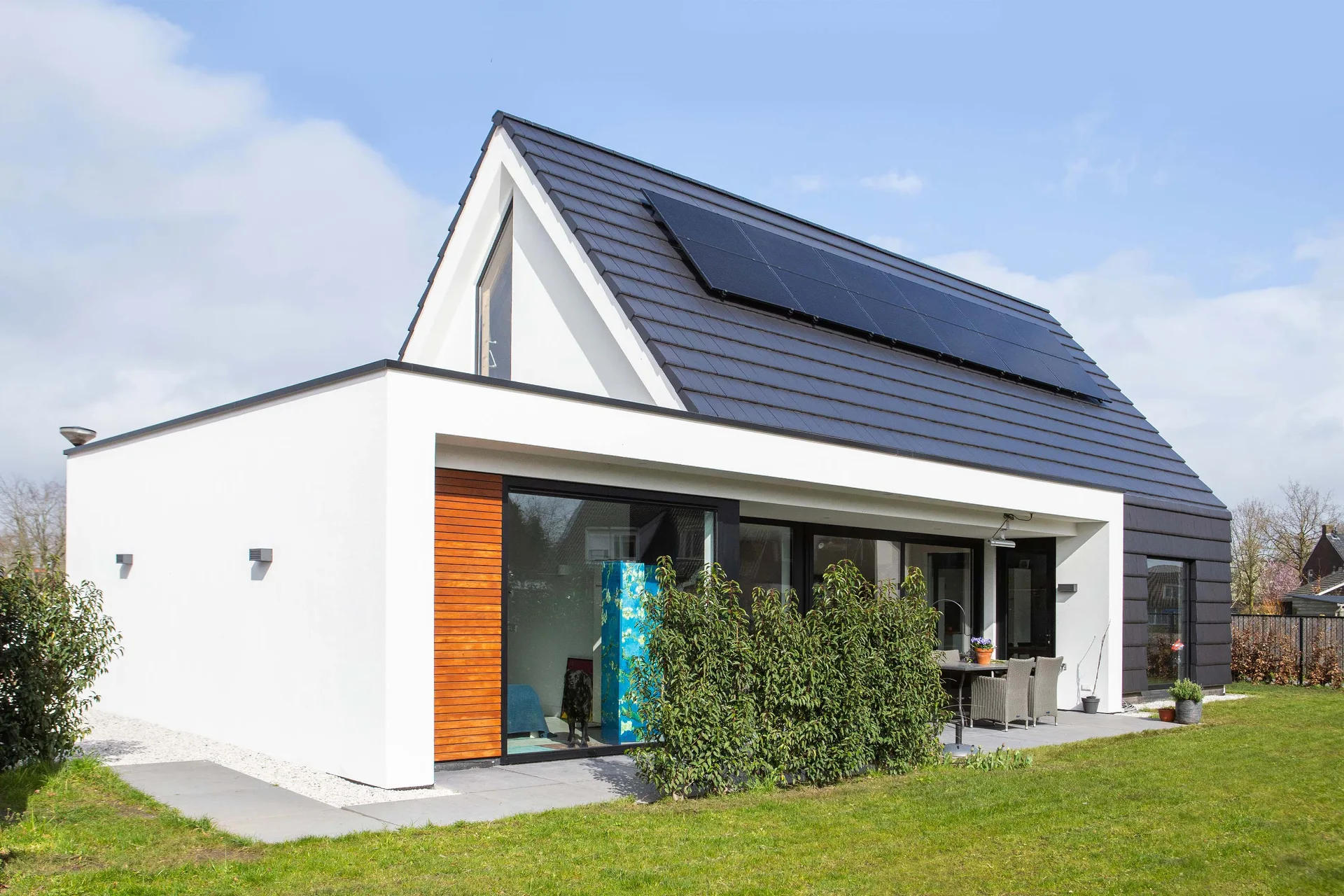 White pitched-roof house with glazing and a garden terrace.