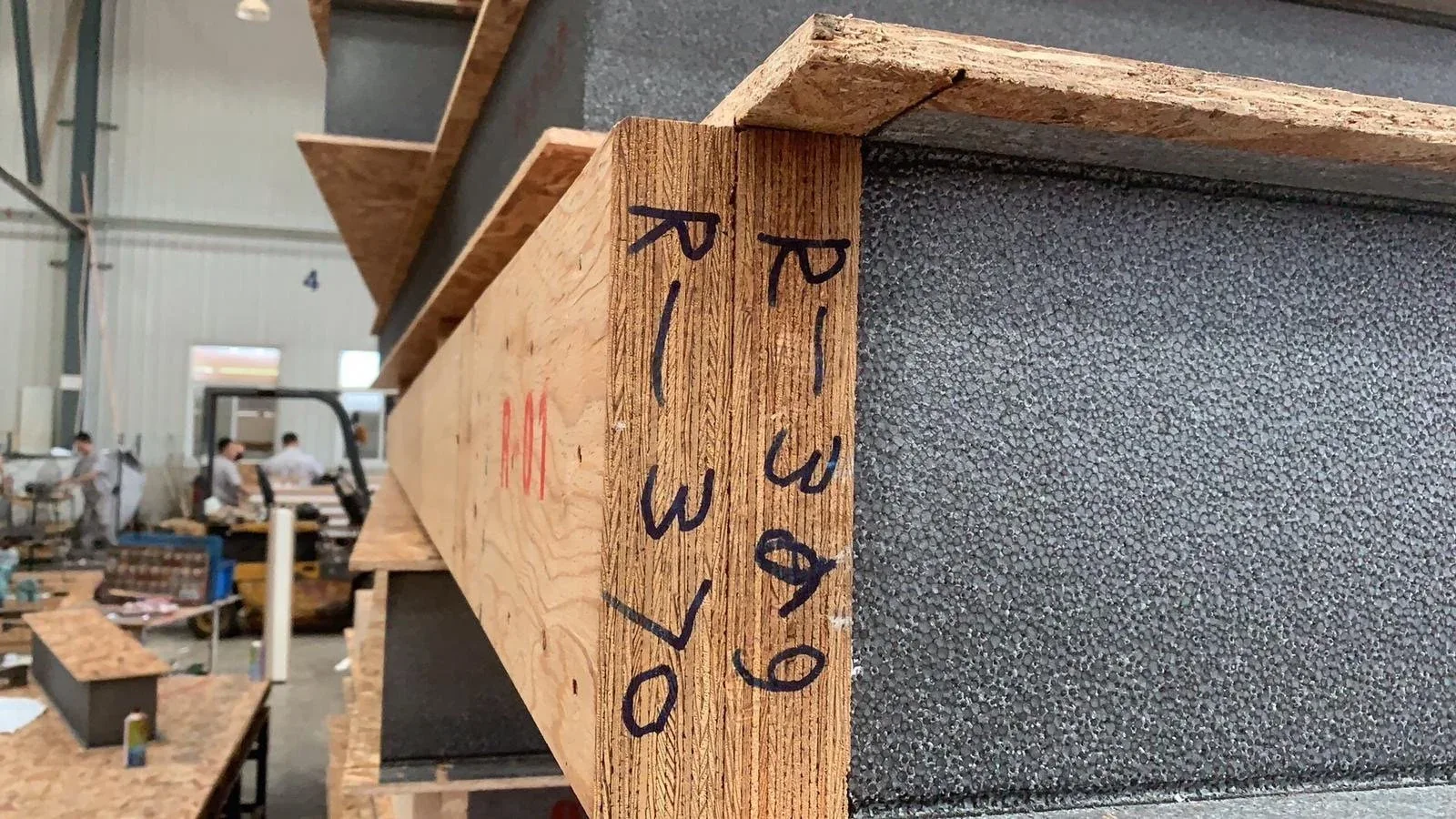 SIP sample showing OSB facings, a grey insulation core and a marked timber edge