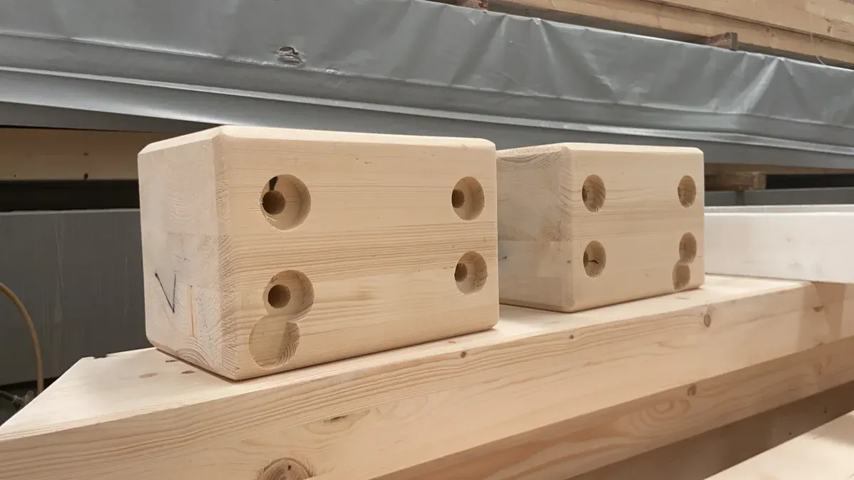 Timber connection components with drilled holes on a factory work surface.